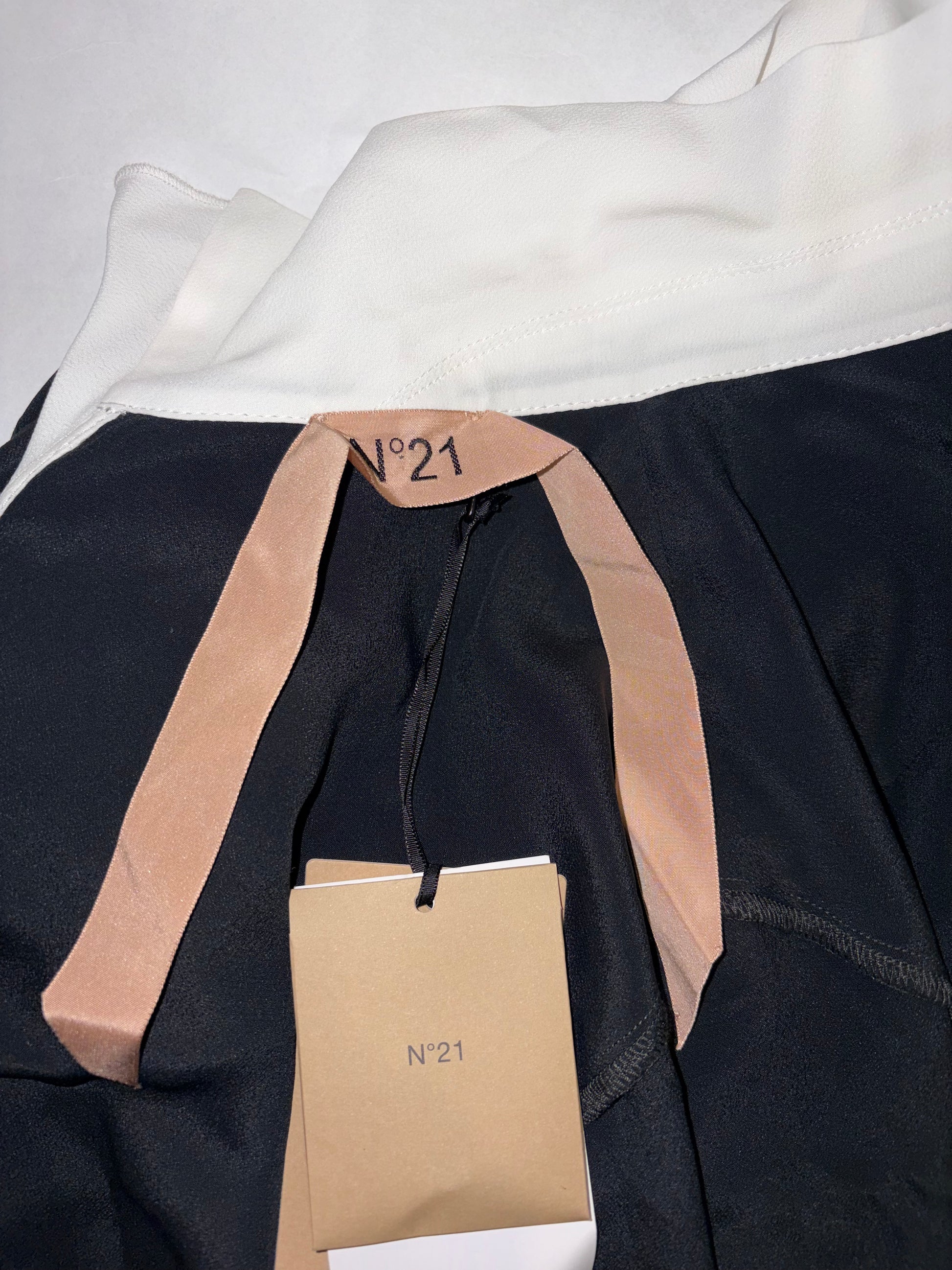 Close-up of a black garment with beige accents and a visible brand tag on a white background